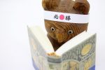 必勝のハチマキをした本を読む木彫りのクマ